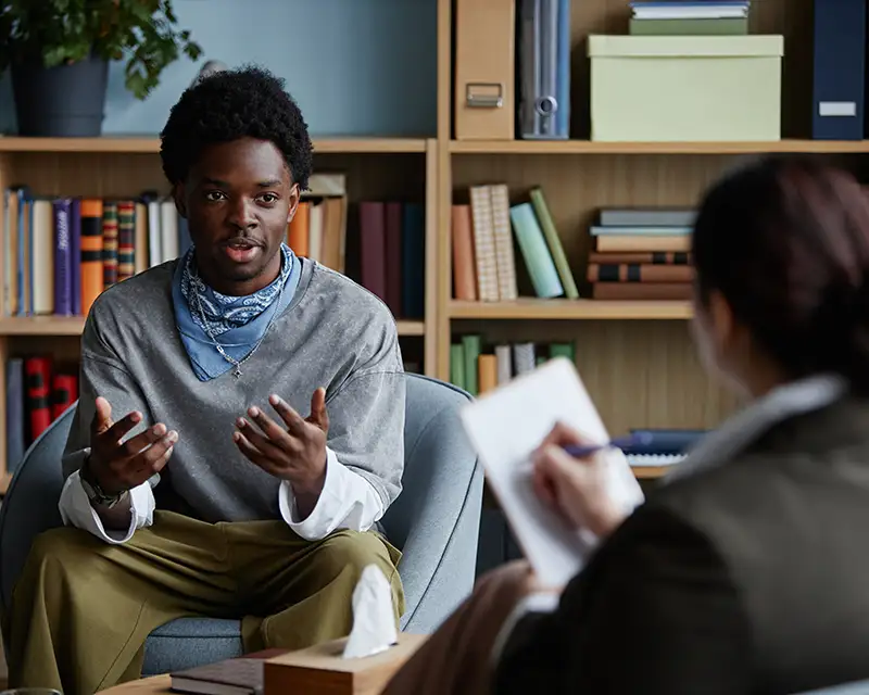 a teenage boy gestures while talking to his therapist